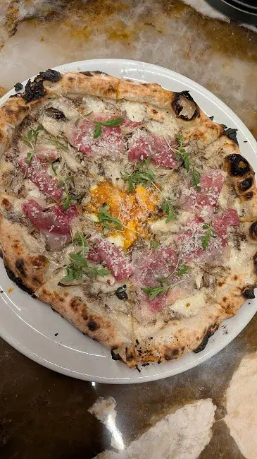 Wagyu Bismarck pizza with mozzarella, parmigiano, wagyu pancetta, truffle paste, Japanese mushroom, and egg.